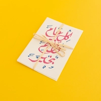 بطاقة معايدة مع ظرف بعبارة "كل عام وأنتم بخير" ومزخرفة بالخط العربي بلون وردي
