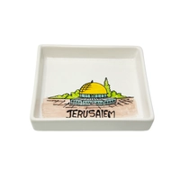 A square white dish decorated with an elaborate hand-painted drawing of the city of Jerusalem and the Dome of the Rock