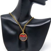 A gold necklace with a resin pendant containing a red flower inside.