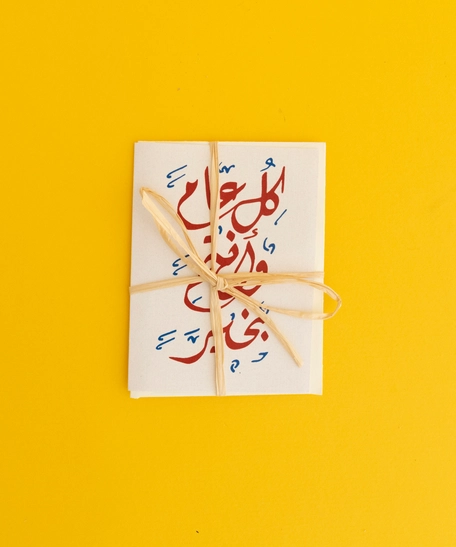 بطاقة تهنئة مع ظرف بعبارة "كل عام وأنتم بخير" مصممة باللون الأحمر وزخرفة الخط العربي - صغير